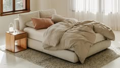 a bed sitting on top of a white floor next to a window with curtains and pillows