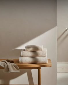 towels are stacked on top of a wooden table next to a lamp and towel rack