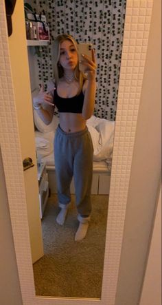 a woman taking a selfie in the mirror while wearing sweatpants and crop top