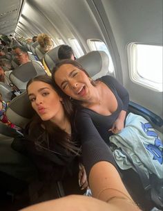 two women are sitting on an airplane with their arms around each other as they look at the camera