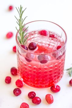 a cranberry cocktail with rosemary garnish in a glass on a white surface