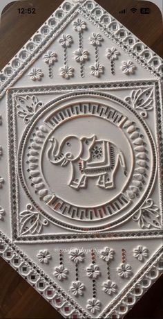 an intricately designed tile with an elephant in the center on a wooden table top