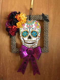 a paper skull hanging on a wall with flowers in the frame and ribbon around it