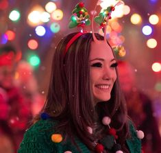 a woman with christmas decorations on her head smiles at the camera while standing in front of brightly colored lights