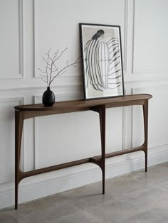 a wooden table with a vase on it next to a painting and a framed photograph