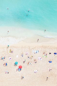 an aerial view of people on the beach with umbrellas and water in the background