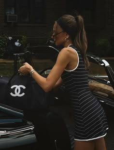 a woman carrying a black chanel bag in her hand while standing next to a motorcycle