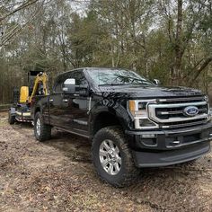 a black truck parked in the woods next to a yellow bulldozer and some trees