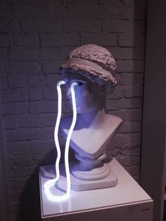 a white bust with a hat on it's head is lit up by neon lights