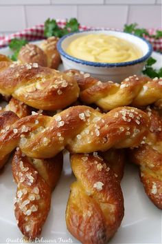 several pretzels on a white plate with mustard dip in the middle and garnished with parsley