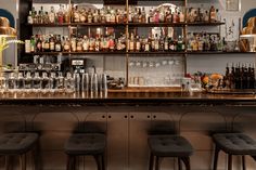 a bar with stools and shelves filled with liquor bottles on the wall behind it