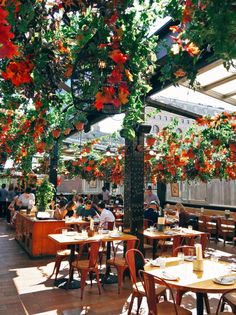 an outdoor restaurant with tables and chairs covered in orange flowered hanging baskets on the ceiling