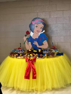 a table topped with a yellow tulle skirt and a snow princess cake topper