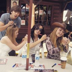 four people sitting at a table with one holding up a straw and the other sticking out her tongue