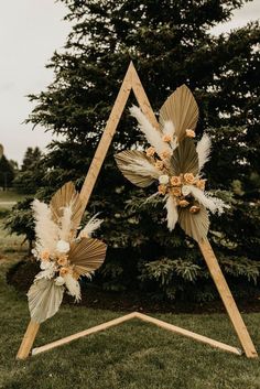 a wooden triangle with flowers and feathers on it sitting in the grass next to a tree