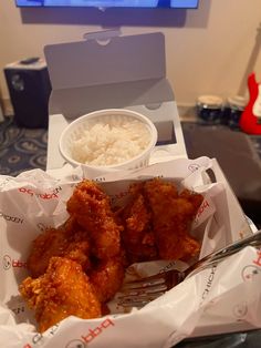 chicken wings and rice in a box on a table next to a flat screen tv