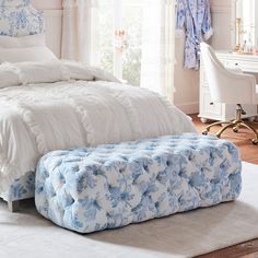 a white bed with blue and white comforter in a bedroom next to a window