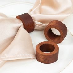 two wooden napkin rings sitting on top of a white plate next to a satin cloth