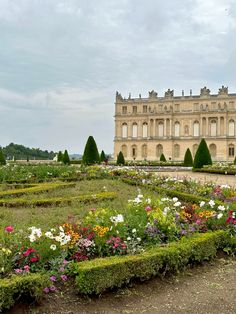 a large building with lots of flowers in front of it and hedges around the perimeter