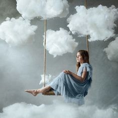 a woman sitting on a swing in the clouds