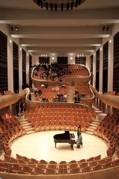 an auditorium filled with lots of seats and a man sitting at a piano in the center