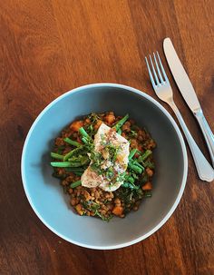 a blue bowl filled with food next to a fork and knife