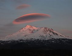 a large mountain covered in snow under a cloudy sky with an orange cloud above it