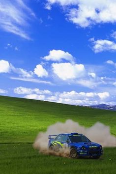 a blue car driving on top of a lush green field under a blue cloudy sky