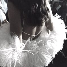 the back of a woman's head with feathers around her neck and hands on her hips