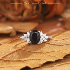 a black and white diamond ring sitting on top of a leaf covered ground with leaves around it