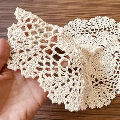 a hand is holding two pieces of crocheted doily