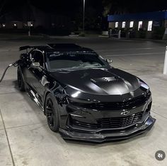 a black chevrolet camaro is parked in a parking lot at night with its hood up