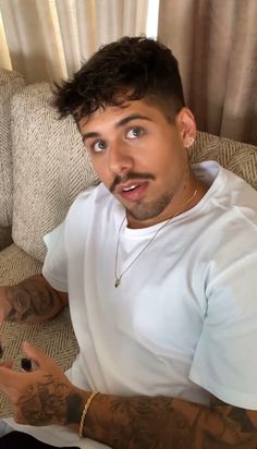 a man sitting on top of a couch holding a cell phone in his hand and looking at the camera