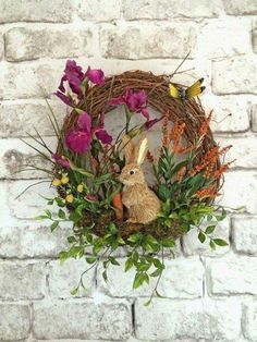 a wreath with flowers and a bunny in it is hanging on the wall next to a brick wall