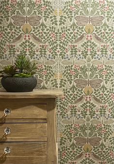 a wooden dresser sitting next to a wall with a plant on top of it in front of a patterned wallpaper