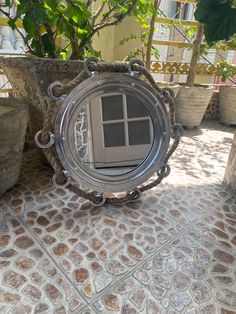 a mirror sitting on top of a stone floor next to potted plants and trees