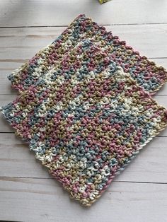 two crocheted dishcloths sitting on top of a white wooden table next to each other