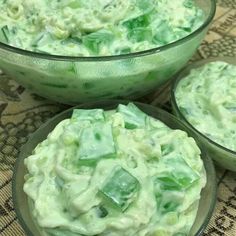 three glass bowls filled with green food on top of a cloth covered tablecloth,