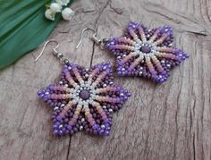 two purple and white beaded earrings sitting on top of a wooden table next to flowers