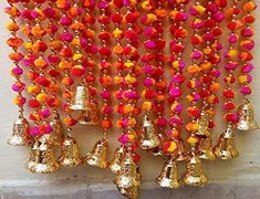 a bunch of bells hanging on the side of a wall with orange and pink pom poms