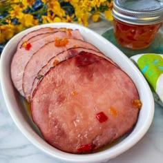 ham slices in a white bowl next to a jar of honey and napkins on a marble table