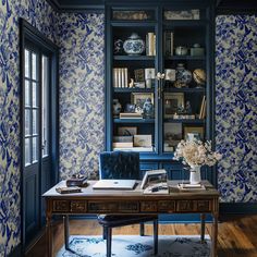 a room with blue and white wallpaper, bookshelves and a wooden desk