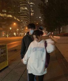 a man and woman walking down the sidewalk at night with masks covering their faces from the sun