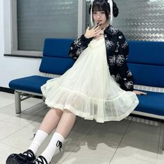 a woman sitting on a blue bench wearing a white dress and black shoes with her legs crossed