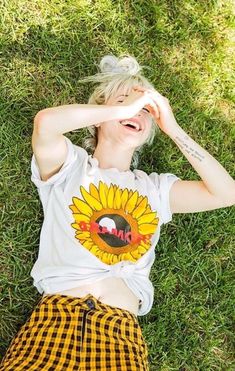 a woman laying in the grass with her hands on her head and wearing a sunflower t - shirt