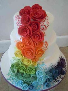 there is a multi layer cake with roses on the top and bottom, decorated in rainbow colors