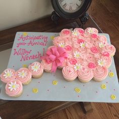 cupcakes with pink frosting and white flowers are on a table next to a clock