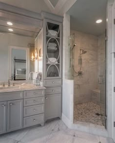 a large bathroom with marble counter tops and gray cabinets, along with a walk in shower