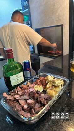 there is a man cooking food in the kitchen with a glass on the counter next to it