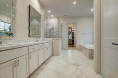 a large bathroom with white cabinets and marble counter tops, along with a walk in shower